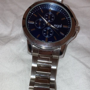 Silverfärgad klocka från Regal - Snygg silverfärgad klocka från Regal med blå urtavla och flera små urtavlor för extra funktioner. Klockan har en robust metallarmband och kommer i originalförpackning. Perfekt för den stilmedvetna!