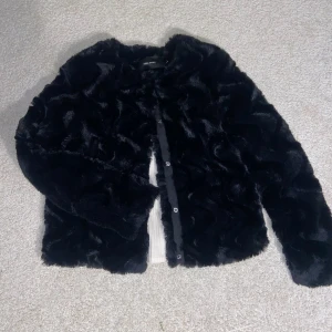Svart pälsjacka med knappar - Säljer en snygg svart pälsjacka med knappar framtill. Jackan har en mjuk och fluffig textur som ger en lyxig känsla. Perfekt för att hålla sig varm och stilren under kyliga dagar💕💕💕