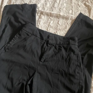 Svarta kostymbyxor från Lindex - Snygga svarta kostymbyxor från Lindex med en klassisk design. De har en dragkedja och knapp framtill för enkel stängning. Perfekta för en stilren look.