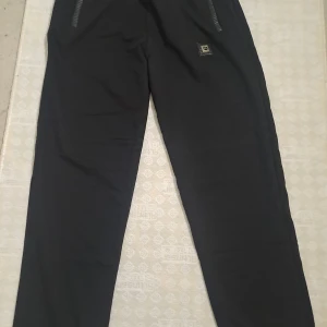 Svarta byxor med dragkedja tränings byxa  - Snygga svarta byxor med dragkedja vid fickorna. Perfekta för en avslappnad stil. Byxorna har en enkel design med en liten logga på sidan.