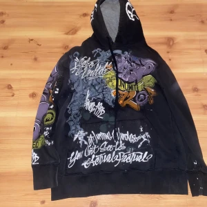 Svart hoodie från Ecko Unltd - Cool svart hoodie från Ecko Unltd med graffiti-inspirerat tryck i flera färger. Hoodien har en stor ficka fram och en justerbar huva. Skriv om du har några frågor. Pris kan diskuteras 