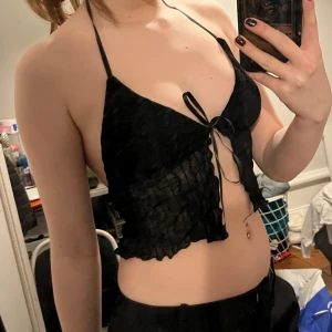 Svart spetslinne - Snygg svart spetslinne med knytning framtill och halterneck-design. Toppen är croppad och har en öppen rygg. 🤗