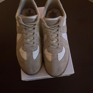 Margielas - Snygga margielas.kombination av beige och vit. Skorna har snörning och är tillverkade i mocka och syntetmaterial. Perfekta för en trendig och avslappnad stil.