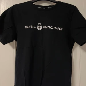 Svart t-shirt från Sail Racing - Snygg svart t-shirt från Sail Racing med vit logga på bröstet. Perfekt för en avslappnad stil. Kortärmad och tillverkad i mjukt material.