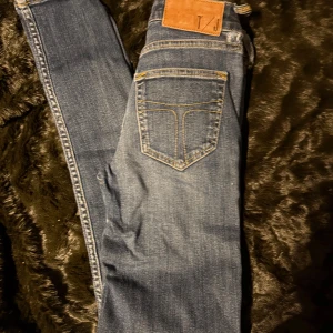 Blå jeans från Tiger Of Sweden  - Snygga blå jeans från Tiger Of Sweden med klassisk femficksdesign och knappgylf. Tillverkade i Italien med detaljer som kontrastsömmar och en läderpatch på baksidan. Perfekta för en avslappnad stil.