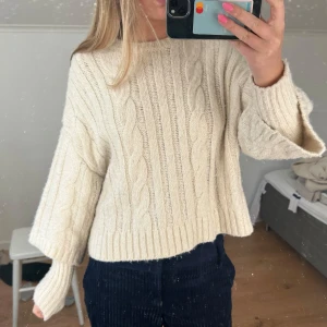 Beige stickad tröja - Säljer en mysig beige stickad tröja med kabelstickat mönster. Tröjan har långa ärmar och en croppad passform som ger en trendig look. Perfekt för kyligare dagar!