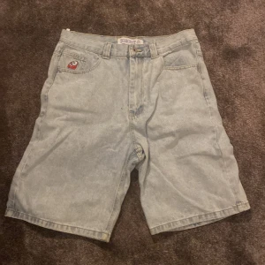 Ljusblå jeansshorts från polar big boys - Säljer ett par ljusblå jeansshorts med en cool patch på framsidan. Shortsen har en klassisk femficksdesign och bälteshällor. Perfekta för en avslappnad stil.
