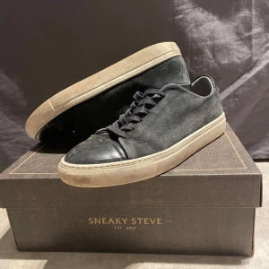 Svarta sneakers från Sneaky Steve original pris 1500kr - Snygga svarta sneakers från Sneaky Steve med en stilren design. Skorna har en svart ovandel i mocka och en tå i skinn, vilket ger en cool kontrast. De har en vit sula och klassisk snörning. Perfekta för en avslappnad stil.