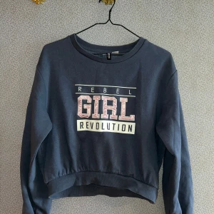 Blå sweatshirt med tryck  - Säljer en blå sweatshirt med texten 'Rebel Girl Revolution' i vitt och rosa på framsidan. Tröjan har en croppad passform och långa ärmar. Perfekt för en avslappnad stil!