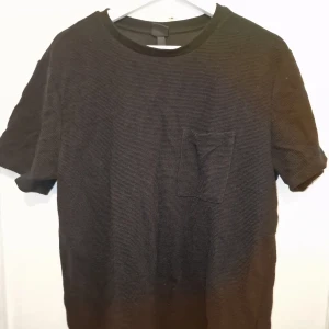 Svart ribbad t-shirt med bröstficka - Säljer en stilren svart t-shirt med ribbad textur. Perfekt för en avslappnad look. T-shirten är använd vid 1 tillfälle. Garderobsrensning så kika gärna på övriga auktioner. 