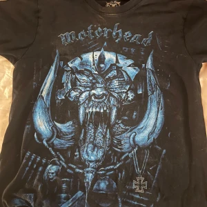 Svart Motörhead t-shirt från Rockvolution - Säljer en svart t-shirt från Rockvolution med ett stort, blått tryck av Motörhead på framsidan. T-shirten är S men passar XS också, och har korta ärmar. Perfekt för fans av bandet!, den har även lite blekning vid halskragen men inget man tänker på💕