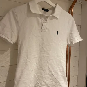 Vit pikétröja från Ralph Lauren - Säljer en klassisk vit pikétröja från Ralph Lauren med den ikoniska broderade logotypen på bröstet. Tröjan har korta ärmar och en stilren krage med knappar. Perfekt för en avslappnad och stilren look. passar xs!