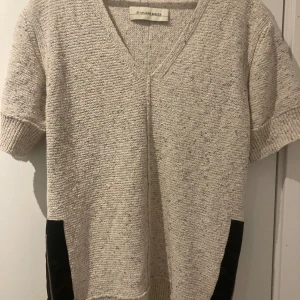 Beige stickad tröja från By Malene Birger - Säljer en snygg beige stickad tröja från By Malene Birger. Tröjan har en v-ringad design och korta ärmar, perfekt för en stilren look. Tillverkad i en blandning av bomull, polyester och linne för en mjuk och bekväm känsla.