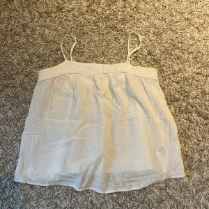 Vit ärmlös topp från H&M - Säljer en söt vit ärmlös topp från H&M med tunna axelband. Toppen har en luftig passform och är perfekt för varma dagar. Den är tillverkad i ett lätt och bekvämt material. Perfekt att matcha med jeans eller kjol för en avslappnad look.