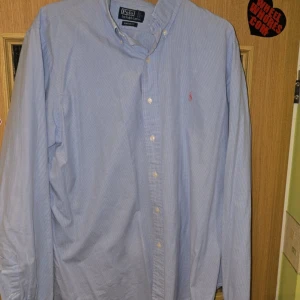 Blå skjorta från Polo Ralph Lauren - Säljer en snygg blå rutig skjorta från Polo Ralph Lauren i storlek XL. Skjortan har långa ärmar och en klassisk krage med knappar. Den är broderad med det ikoniska rosa logotypen på bröstet. Perfekt för både vardag och fest! 💙 Skick: 7.5/10