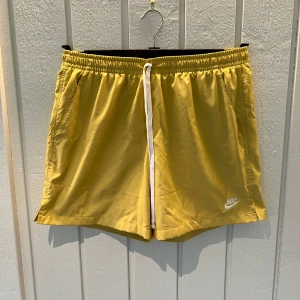 Gula shorts från Nike - Säljer ett par snygga gula Nike-shorts i storlek L. Perfekta för sommaren med en bekväm passform och elastisk midja med dragsko. De har en klassisk design med Nike-loggan på benet. Perfekta för både träning och avslappnade dagar! Skick: nyskick.