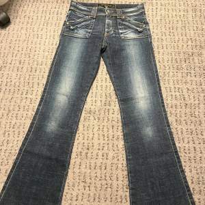 Säljer dessa sjukt fina jeans med detaljer på både baksidan och framsidan. Dessa jeans har inga besvär, de är som helt nya jeans från 2000-talet 💞 Orginal priset är runt 1 300kr! midja: 26 lår: 22cm innerben: 72 cm 