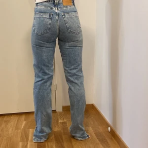 Blå jeans från Zara - Säljer ett par snygga blå jeans från Zara i storlek 32. De har en cool distressed look med slitningar och är högmidjade för en bekväm passform. Perfekta för en avslappnad stil och kan matchas med allt från sneakers till klackar.