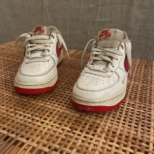 Nike Air Force i vitt och rött - Säljer ett par Nike Air Force i vitt med röda detaljer. Skorna har en klassisk design med snörning och är i välanvänt skick. Perfekta för vardagsbruk eller för att ge din outfit en sportig touch. Kommer med originalkartong.