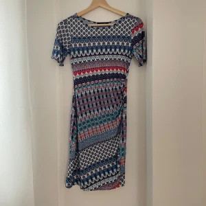 Mönstrad klänning från SisterS Point - Säljer en superfin mönstrad klänning från SisterS Point i storlek XS. Klänningen har ett färgglatt mönster i blått, rött och grönt med korta ärmar. Perfekt för både vardag och festliga tillfällen. Den är i mycket bra skick och redo för en ny ägare!