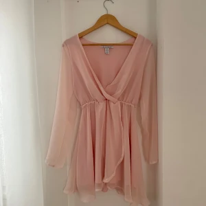 Ljusrosa omlottklänning från NLY Trend - Säljer en superfin ljusrosa omlottklänning från NLY Trend i storlek 34. Klänningen har långa ärmar och en v-ringad design som ger en elegant touch. Perfekt för vår och sommar! 💖