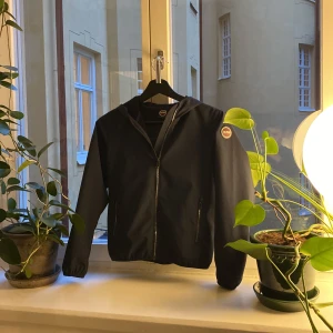 Marinblå vindjacka med huva - Säljer en stilren marinblåa vindjacka från Colmar. Jackan har en praktisk huva och dragkedja framtill. Perfekt för höst och vår, med en enkel och modern design. Passar både till vardags och lättare utomhusaktiviteter.