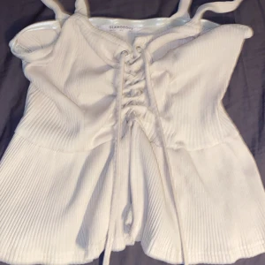 Beige topp  Glamorous - Säljer en superfin beige ribbad topp från Glamorous i storlek EU 34. Den har snygg snörning framtill och är perfekt för både vardag och fest. Toppen är i mycket bra skick och har en tight passform som framhäver figuren. 