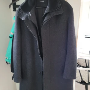 Svart kappa från Zara - Säljer en stilren svart/mörkgrå kappa från Zara i perfekt skick och aldrig använd. Den har en klassisk design med långa ärmar och en diskret dragkedja framtill. Perfekt för höst och vinter. Den har en borttagbar innerväst, jämför bild 4 och 5. Storleken är Large.