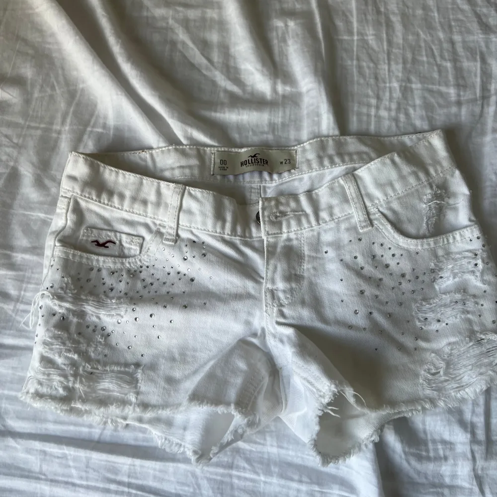 Säljer ett par vita shorts från Hollister i bra skick. De är dekorerade med små pärlor och har en snygg slitning för en avslappnad look. Perfekta för sommardagar på stranden eller en avslappnad dag i stan. De är lågmidjade och har en normal passform.. Shorts.