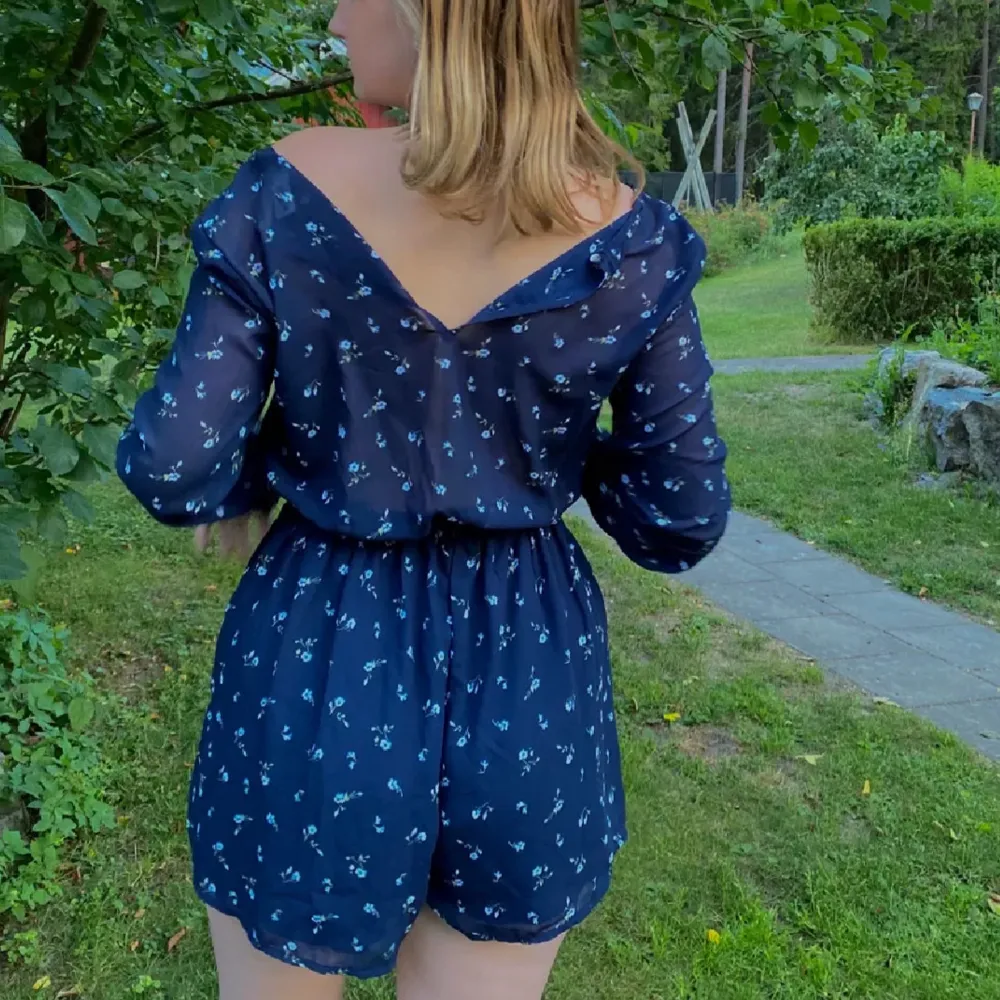 Säljer en superfin blå jumpsuit från Hollister med små blommor. Den har långa ärmar och en omlott-design framtill. Genomskinligt tyg i ryggen. Materialet är lätt och luftigt, vilket gör den bekväm att bära. 💙aldrig använd så toppen skick . Klänningar.