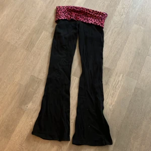 Svarta yoga byxor med leopardmönstrad midja - Säljer ett par svarta byxor med en cool leopardmönstrad midja i rosa och svart. Byxorna har en loose fit och är perfekta för en avslappnad stil. De är i bra skick och passar perfekt för både vardag och fest. 🐆✨