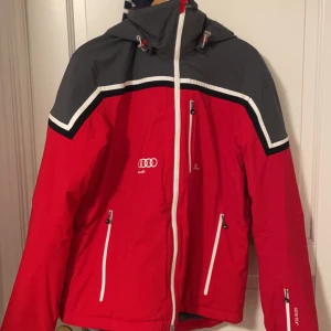Jacka j.lindeberg (skid) - Säljer en snygg röd och grå jacka från J.Lindeberg med Audi-logga. Den har en dragkedja framtill och praktiska fickor. Perfekt för höst och vinter med sitt slitstarka Gore-Tex-material. Jackan har långa ärmar och en justerbar huva. Passar perfekt för både vardag och t.ex att åka skidor med. Använd 1-2 gånger då jag köpte av en annan. Denna jackan fås bara med när man köper AUDI bil.