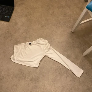 Vit oneshoulder topp från Shein - Säljer en stilren vit oneshoulder topp från Shein i storlek M. Toppen har en lång ärm och är perfekt för både vardag och fest. Materialet är mjukt och bekvämt, vilket gör den idealisk för alla säsonger. Passar perfekt med jeans eller kjol för en chic look!