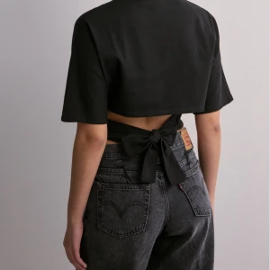 Nelly tröja med knytning i ryggen - Snygg svart croppad topp med korta ärmar och knytband i ryggen. Perfekt för en avslappnad stil eller en utekväll. Toppen är i bra skick och passar till både jeans och kjol.