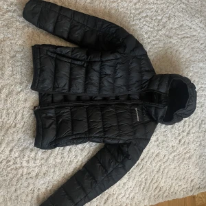 Svart dunjacka från Peak Performance - Säljer en svart dunjacka från Peak Performance i mycket bra skick. Jackan har en stilren design med dragkedja och huva, perfekt för kyliga dagar. Den är varm och bekväm, idealisk för både höst och vinter. Passar perfekt för dig som vill hålla stilen i kylan! Dragkedja kan vara lite trög och hoppa ibland där av priset