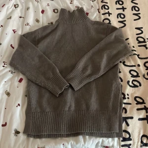 Brun stickad polotröja - Mysig brun stickad polotröja med ribbade detaljer vid ärmslut och nederkant samt slits på båda sidorna. Perfekt för kyliga dagar och ger en stilren look. Tröjan har långa ärmar och en hög krage som håller dig varm. Passar både till vardags och mer uppklädda tillfällen.