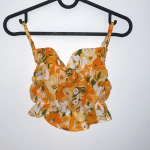 Blommig gul och vit linnetopp - Säljer en superfin blommig linnetopp i gult och vitt med gröna detaljer. Toppen har smala axelband och en söt volangdetalj längst ner. Perfekt för sommardagar och festivaler! 🌼