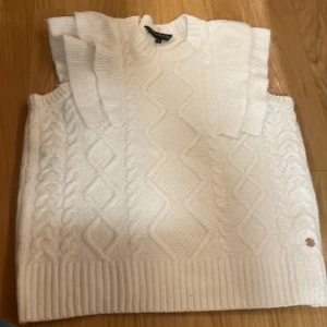 Vit stickad ärmlös tröja från Pernilla Wahlgren - Säljer en superfin vit stickad tröja från Pernilla Wahlgren. Den är ärmlös med ett snyggt flätmönster och ribbade kanter. Perfekt för lager-på-lager under hösten eller vintern. Passar både till vardags och fest! 🧶✨Använd cirka 2 gånger 🥰