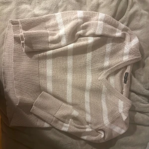 Beige och vit randig tröja från Stockh LM - Mysig beige och vit randig tröja från Stockh LM i storlek S. Perfekt för höst och vinter med sin stickade design och långa ärmar. Tröjan har en bekväm passform och ribbade muddar vid ärmslut och nederkant. Ett måste för garderoben!