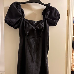 Svart klänning - Säljer denna söta klänning då den inte passar längre. Otroligt fin med sin öppning under brösten och knytning. Slutar ungefär precis över knäna på mig och jag är 158 cm. Köpare står för frakt ❤️