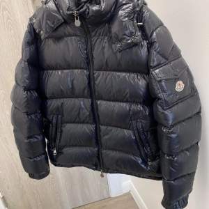 Säljer en snygg svart dunjacka från Moncler i mycket bra skick. Jackan har en glansig finish och är perfekt för vintern. Den har en dragkedja framtill och långa ärmar. Moncler-loggan syns på ärmen. Perfekt för kalla dagar! ❄️