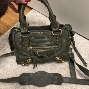 Khakigrön väska  - Säljer denna jättefina väska då den inte kommer till användning! En otroligt snygg färg med gulddetaljer💕finns slitningar på väskan o handtaget men absolut inget som påverkar väskans användning! 