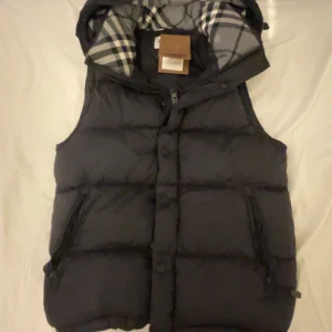 Svart burberry väst/jacka - Säljer en svart burberry väst i mycket bra skick. Den har avtagbara armar Västen har dragkedja och knappar framtill samt två fickor med dragkedja. Perfekt för höst och vinter! Skriv vid minsta fundering. strl S