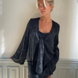 Svart blus med knytdetalj - Snygg svart blus med  knyt framtill. Den har långa ärmar och en elegant, mörk ton. Perfekt för både vardag och festliga tillfällen. Blusen är i ett mjukt och bekvämt material som ger en stilren look