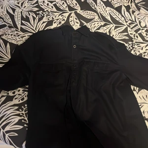 BLÅ skjorta från GANT - Säljer en stilren svart skjorta från GANT i storlek M. Skjortan har långa ärmar och knappar framtill. Perfekt för både vardag och festliga tillfällen. Passar bra till höst- och vintergarderoben. 