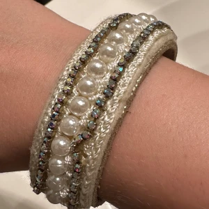 Lyxigt  armband med pärlor och strass - Snyggt beige armband från Waitz med pärlor och glittrande strassdetaljer. Armbandet har en justerbar knäppning med tryckknappar och en mjuk insida i läder för bekväm passform. Perfekt för att ge en elegant touch till din outfit! Går att ställa till 3 olika storlekar. Nypris 900kr