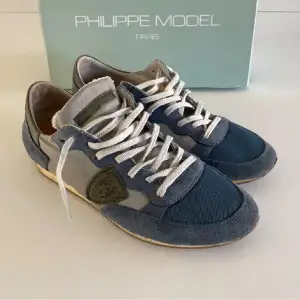 Säljer ett par snygga Philippe Model sneakers i blått och grått. Skorna har en cool design med snörning och är i mycket bra skick. Perfekta för både vardag och festliga tillfällen. Kommer i originalkartong.