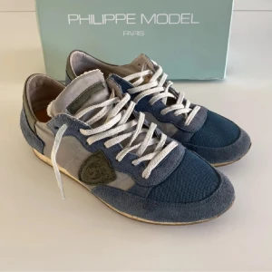 Philippe Model sneakers - Säljer ett par snygga Philippe Model sneakers i blått och grått. Skorna har en cool design med snörning och är i mycket bra skick. Perfekta för både vardag och festliga tillfällen. Kommer i originalkartong.