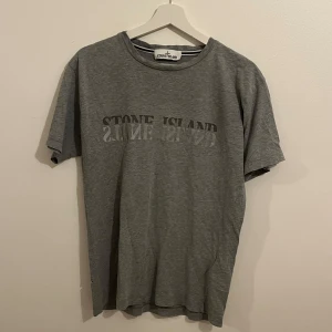  Stone Island T-shirt - En grå T-shirt från märket Stone Island, den är i storlek M, finns ett ganska stort hål på sidan av T-shirten som ni ser på sista bilden därav billigare pris (syns inte lika mycket vid användning). Skriv vid frågor!