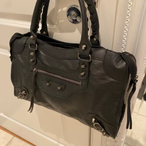 Väska  - Säljer en snygg svart med coola nitar och dragkedja. Perfekt för både vardag och fest! Den har en stilren design med flätade handtag och detaljer som ger en edgy look. Väskan är i mycket bra skick och passar till alla outfits.